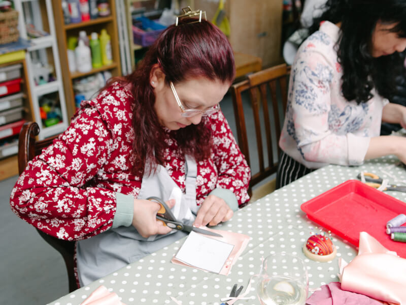 A person sits at a table, cutting round a paper pattern pinned to fabric